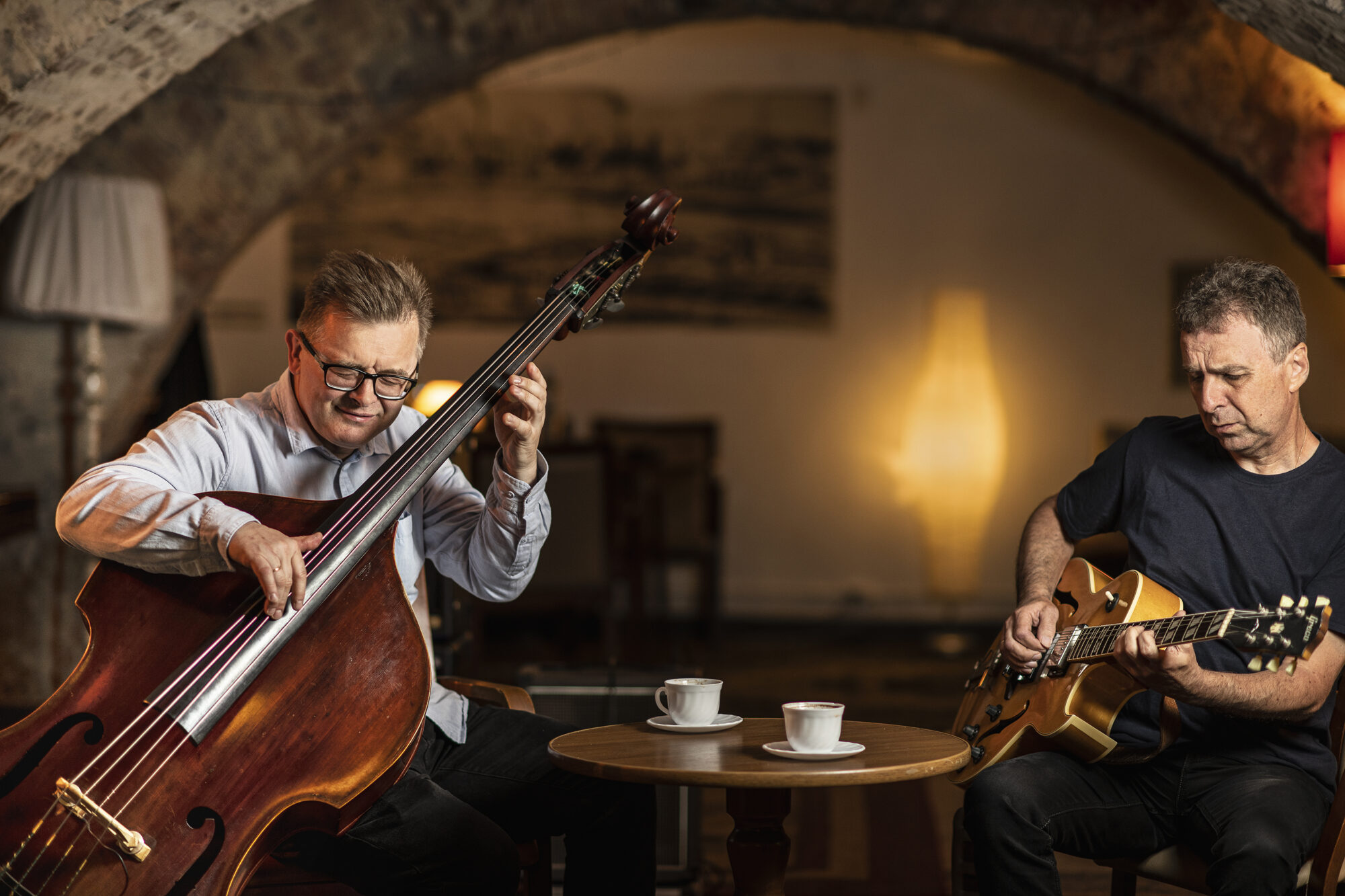 Na zdjęciu muzycy Bohdan Lizoń i Grzegorz Piętak siedzą przy stoliku w kawiarni i grają na instrumentach