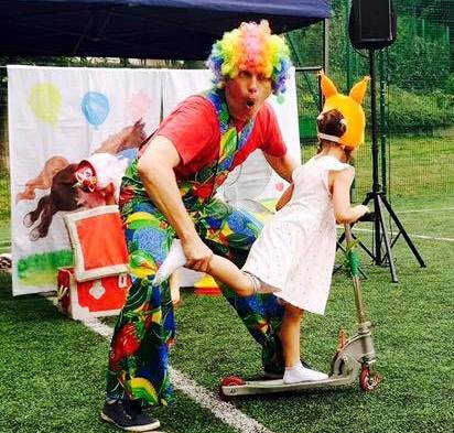 Na zdjęciu przebrany za kolrowego klauna aktor bawi się z dziećmi