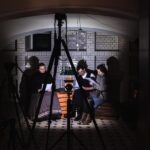 Na pierwszym planie urządzenia do rejestracji obrazu i dźwięku. W tle pomiedzenie w którym siedzi troje aktorów w strojach scenicznych. Foto Monika Bilska