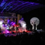 Na zdjęciu widok ogólny amfiteatru podczas koncertu Rock Noc. Widać scenę z kolorowymi światłami, na niej zespół oraz ciemne sylwetki fanów i biały balon SCK. Foto Monika Bilska