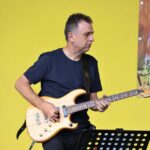 Na zdjęciu zbliżenie na postać znakomitego gitarzysty - Bohdana Lizonia. Muzyk gra na gitarze na tle żółtej ściany amfiteatru. Foto Monika Bilska