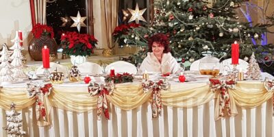 Piosenkarka Bernadeta Kowalska ubrana na biało, przy świątecznym, zastawionym stole na tle choinki.