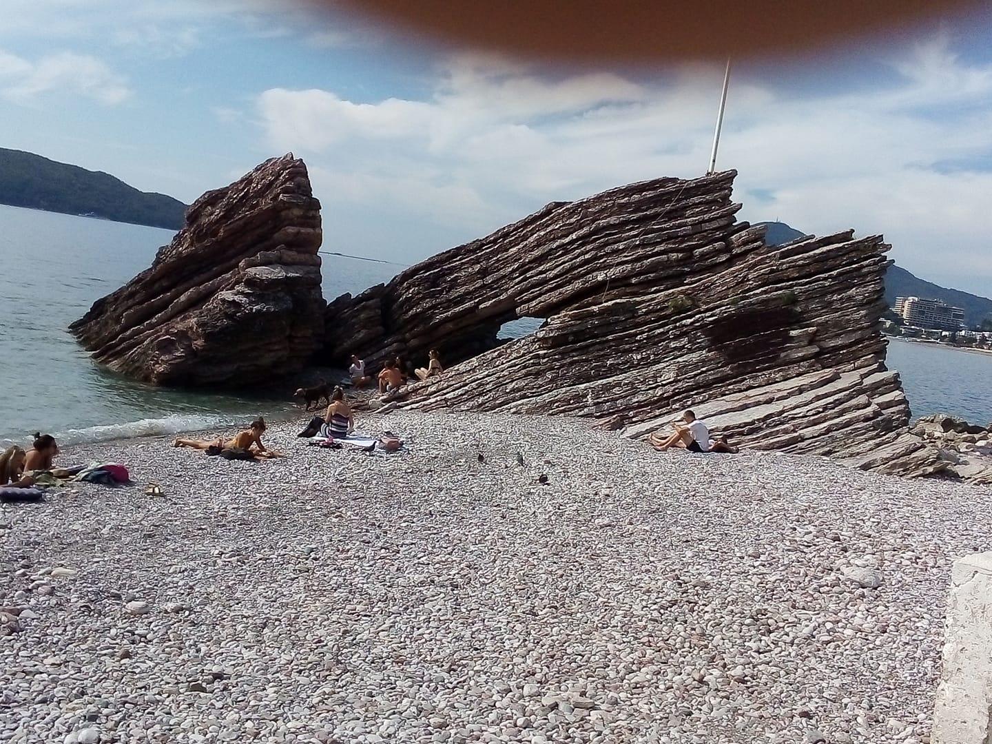 Na zdjęciu bałkańska, skalista plaża i morze. Na plaży opalają się ludzie, w tle skały