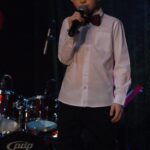 Szymon Wantuła w białej koszuli i muszce śpiewa do mikrofonu na scenie SCK- Bytków