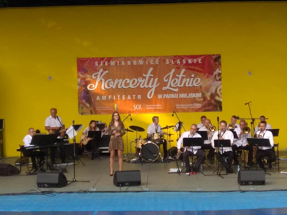 Widok na scenę amiteatru na któej w ramach Letnich Koncertów występują muzycy orkiestry Siemion Band. Towarzyszy im wokalistka Zuzanna Krupa.