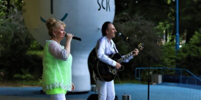 Zbliżenie na sylwetki muzyków zespołu Metrum. Teresa ma na sobie żóltą tunikę i białe spodnie. Ubrany na biało Marek Halup śpiewa i gra na gitarze. Foto Monika Bilska