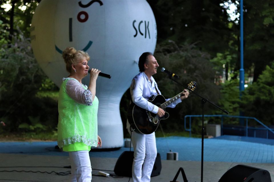 Zbliżenie na sylwetki muzyków zespołu Metrum. Teresa ma na sobie żóltą tunikę i białe spodnie. Ubrany na biało Marek Halup śpiewa i gra na gitarze. Foto Monika Bilska