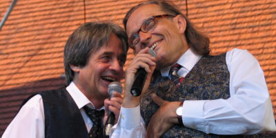 Zdjęcie przedstawia uśmiechniętych Ecika i Masztalskiego podczas występu przed publicznością