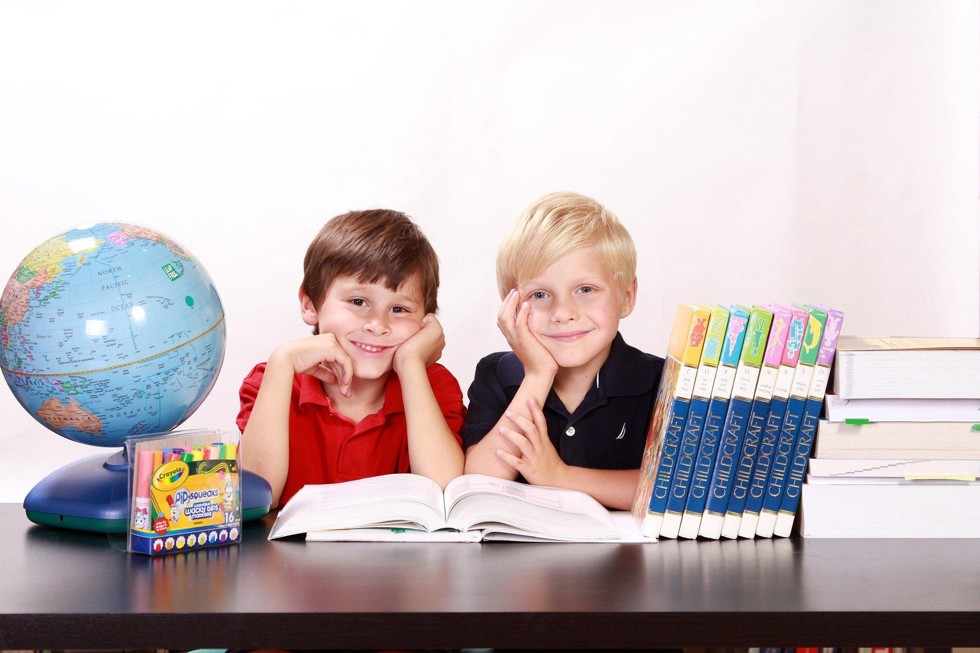 dwóch chłopców przy biurku. Obok stoją globus i książki