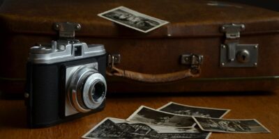 Na zdjęciu aparat fotograficzny, zdjęcia oraz stara, brązowa walizka