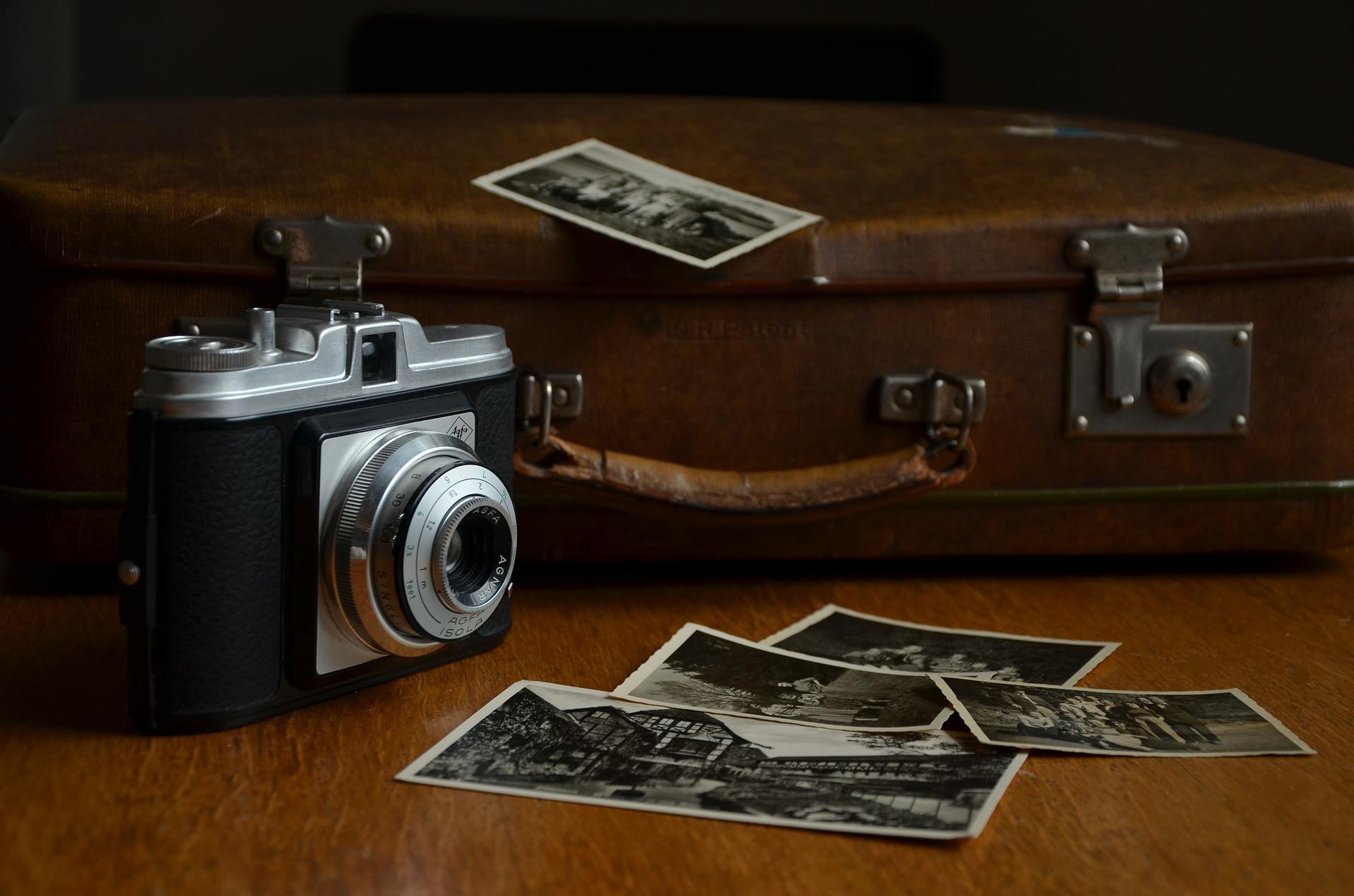 Na zdjęciu aparat fotograficzny, zdjęcia oraz stara, brązowa walizka