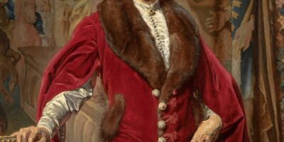 Zdjęcie przedstawia portret Józefa Ciechońskiego. Widzimy mężczyznę w stroju historycznym w kolorze czerwonym
