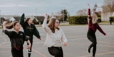 Na boisku szkolnym tańczy grupa młodych dziewcząt, ubranych w stroje sportowe
