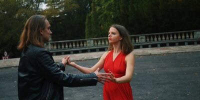Kobietas w czerwonej sukience i mężczyzna w czarnej, skórzanej kurtce tańcą w parku